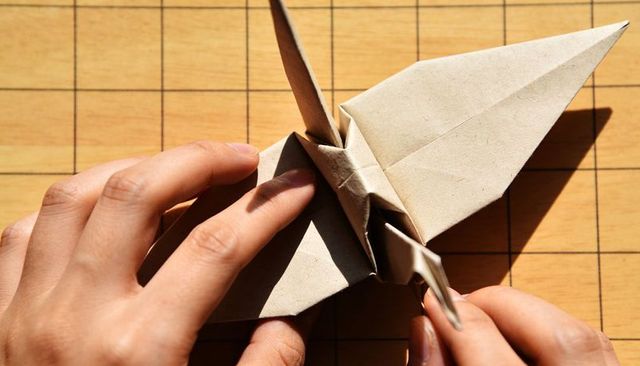 Hands folding origami crane on wooden grid board in warm sunlight