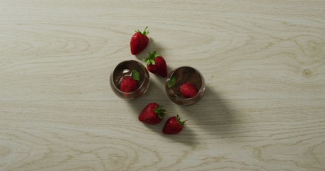 High angle view of fresh strawberries in chocolate cups arranged on a light wooden surface. Suitable for use in culinary blogs, gourmet food advertising, dessert recipe websites, or social media posts showcasing sweet treats and indulgent foods.
