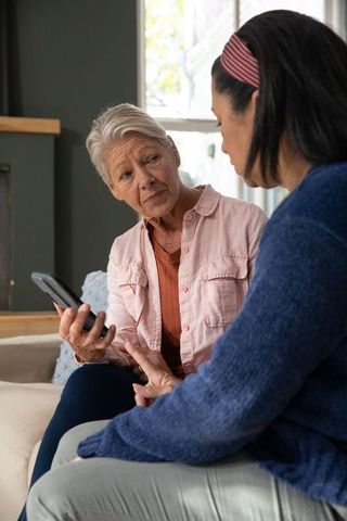 Senior woman showing smartphone to friend on sofa sharing companionship and care