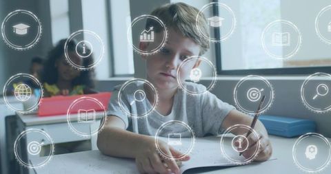 Elementary student concentrating while writing in classroom with digital learning icons
