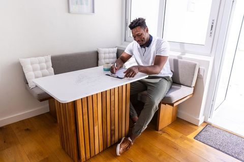 African american man writing at breakfast nook near window, casual home workspace