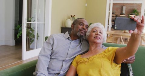 Happy Senior Couple Sitting on Couch Taking Selfie