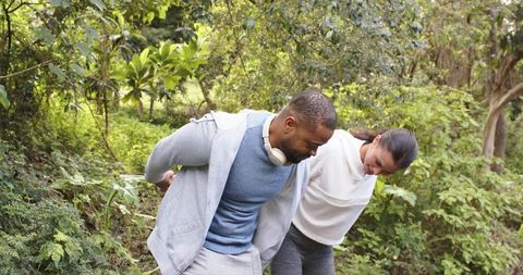 Couple leaning forward examining plants on grassy forest trail wearing hoodies and headphones