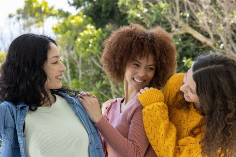Multiracial women laughing and linking arms outdoors, enjoying friendship and sunlight