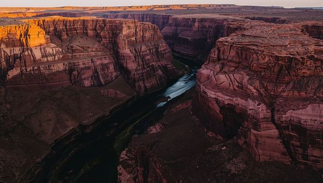 Framing meandering river through sunlit banded sandstone canyon from high vantage at sunset