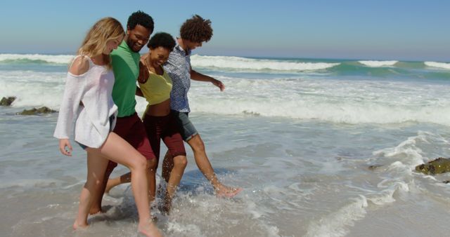 Group of friends having fun walking by ocean waves on sunny beach day, enjoying vacation, splashing in the water. Perfect for promoting tourism, summer vacations, leisure activities, friendship, and outdoor adventures.