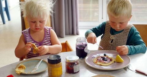 Young siblings eating pancakes with jams at home