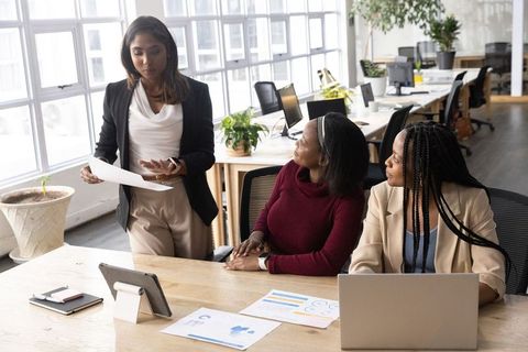Diverse women presenting documents and reviewing charts in modern open-plan office
