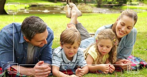 Family lying on blanket exploring wildflowers by pond in sunny park togetherness