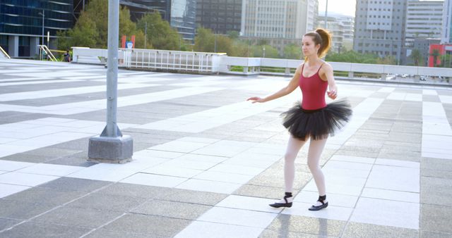 Ballet dancer is practicing on an urban plaza, showing grace and dedication. Her attire includes a black tutu and pointe shoes, highlighting her artistic discipline. Skyscrapers and other modern buildings in the background emphasize the urban environment. This image is ideal for themes of perseverance, the arts, city life, and cultural activities.