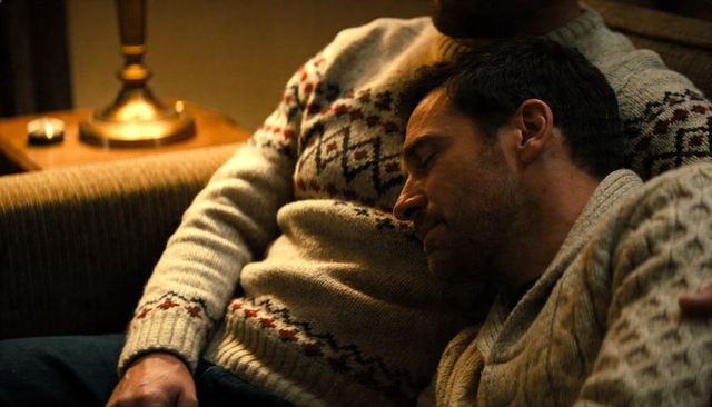 Male couple cuddling on sofa wearing patterned knit sweaters, cozy living room moment