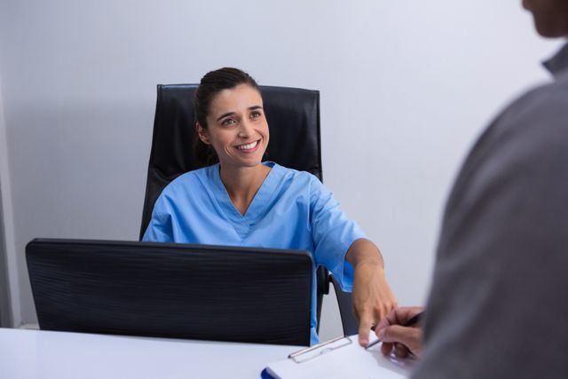 Smiling doctor interacting with patient at desk in clinic