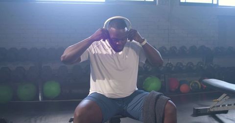 Athlete adjusting headphones on bench before strength training in industrial gym