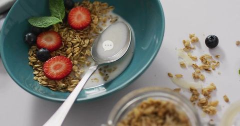 Teal bowl holding granola, milk and fresh berries with spoon and scattered crumbs