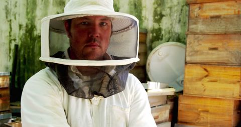 Confident beekeeper in protective suit standing in apiary