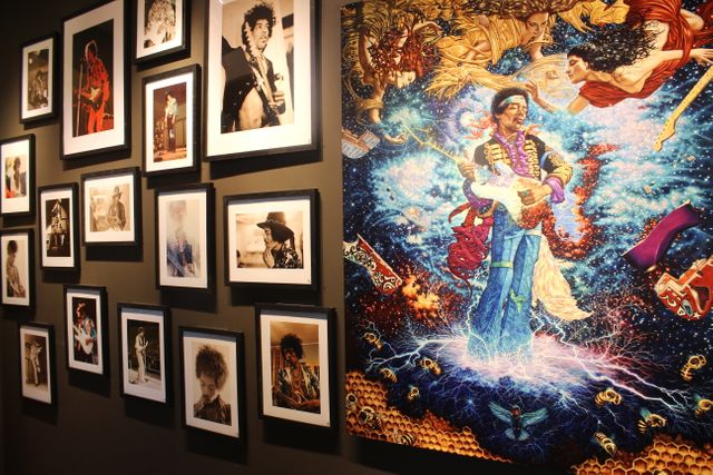 This showcases a combination of black and white photographs and a colorful, detailed painting of Jimi Hendrix. The smaller frames display moments from his career, while the vibrant large artwork depicts Hendrix with cosmic and surreal elements. Ideal for use in content related to music history, legendary musicians, interior decoration, art exhibitions, and cultural references to classic rock music.