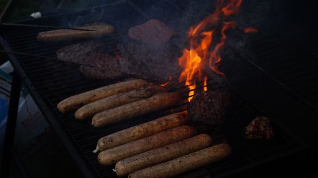 Sausages and burger patties are grilling on an open flame, creating a smoky atmosphere. This image is ideal for illustrating BBQ events, outdoor cooking activities, summer gatherings, or food-related content.
