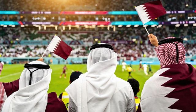Qatari fans waving maroon flags in traditional thawb and ghutra at football match