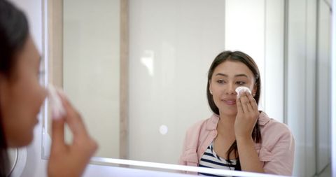 Woman Smiling and Applying Skincare in Bathroom Mirror