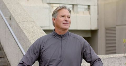 Mature man reflecting in urban plaza wearing gray zip-up pullover, minimalist architecture