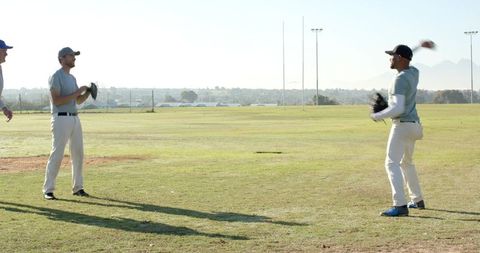 Diverse Male Teammates Practicing Baseball on Sunny Field Throwing Catching Coaching