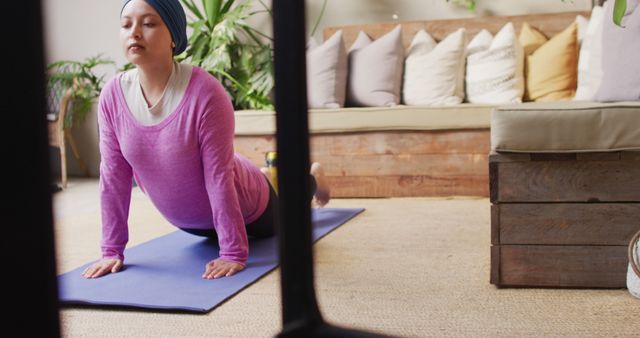 Woman practicing yoga on mat in comfortable living room. Suitable for wellness, fitness, and healthy lifestyle content. Image captures home exercise setting, promoting self-care and mindfulness.