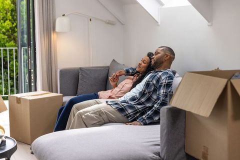Couple relaxing on sofa after moving in, unpacking boxes and enjoying new home