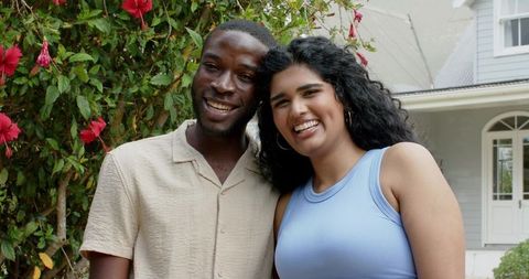 Smiling young couple on front porch with red hibiscus garden, casual summer lifestyle