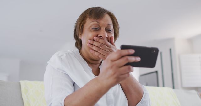 Senior woman showing joyful excitement while looking at smartphone, suitable for themes around technology use by seniors, family connections, or positive emotional responses. Perfect for advertising telecom services, showcasing seniors using tech, or illustrating positive aged care experiences.