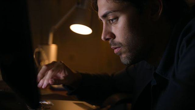 Man Focusing While Working Late on Laptop at Home Desk Under Warm Lamp Glow