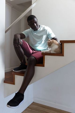 Man relaxing on staircase at home petting ginger cat