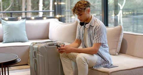 Young man relaxing with smartphone and luggage in modern sitting room