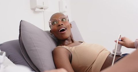 Surprised african woman receiving abdominal ultrasound while reclining on exam bed