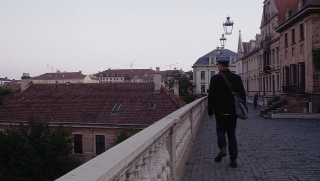 Walking man carrying satchel on historic european terrace at dusk