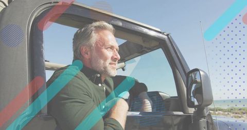 Mature man enjoying coastal road trip leaning from open-top jeep overlooking ocean horizon