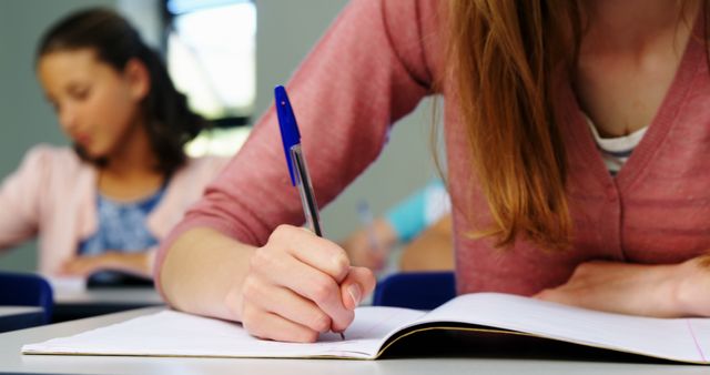 Students writing attentively in notebooks in classroom setting. Perfect for education-related themes, study tips, academic resources, exam preparation materials, and classroom environment visuals.