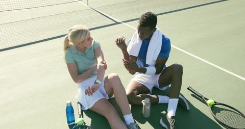 Tennis players resting and inspecting forearms on hard court during sunny outdoor break