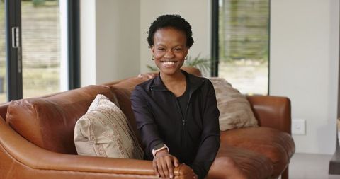 Smiling african american woman on leather sofa with smartwatch in modern living room