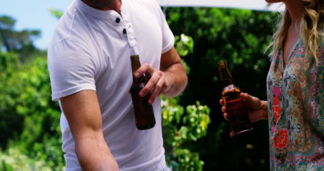 Friends holding beers, enjoying a summer barbecue outdoors. Can be used for advertising social gatherings, summer events, alcohol, or casual lifestyle activities.