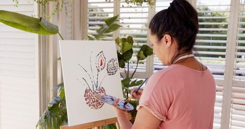 Female artist painting floral canvas at home in daylight