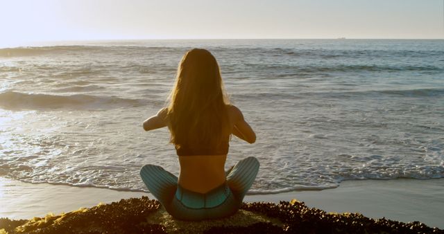 Woman in mermaid costume sitting on beach looking at ocean horizon during sunset. Great for themes related to fantasy, relaxation, summer vacations, coastal living, inner contemplation and nature appreciation.