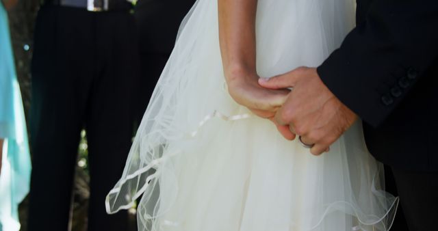 A bride and groom hold hands on their wedding day, showcasing a moment of intimacy and unity. Their clasped hands symbolize the beginning of their journey together as a married couple.