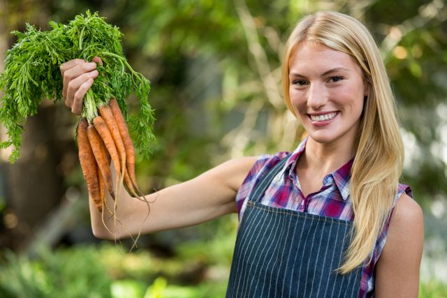 Portrait of beautiful female gardener with fresh organic carrots at garden