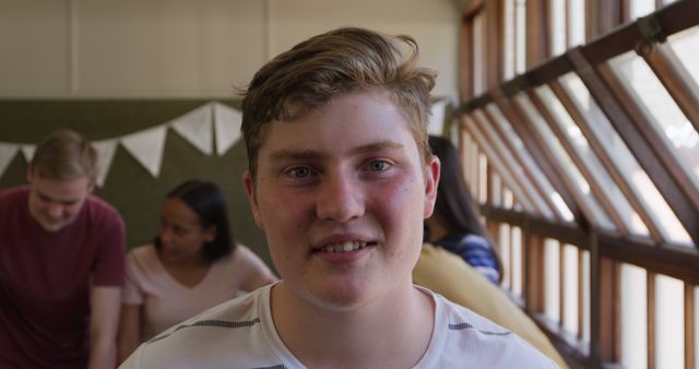 Portrait of happy caucasian teenage boy with brown hair smiling in school classroom. School, learning, adolescence, childhood, summer and education, unaltered.