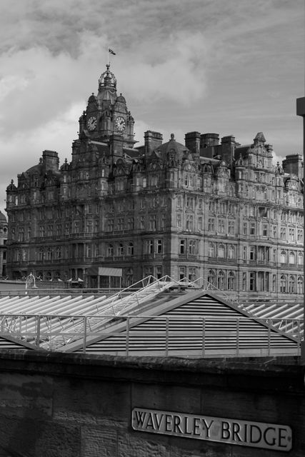Black and white view of an iconic building on Waverley Bridge, showcasing detailed architecture and a prominent clock tower. Perfect for use in travel magazines, historical content, urban photo collections, and architectural showcases highlighting Edinburgh landmarks.