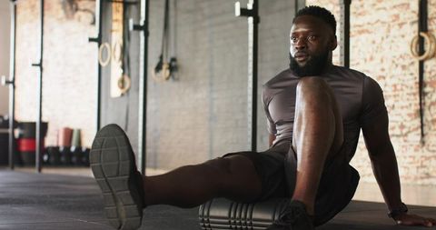 African american athlete recovering with foam roller in gym