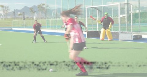 Field hockey forward dribbling toward goal with goalkeeper in protective pads action outdoor