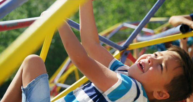 Young boy climbing on jungle gym equipment in outdoor playground on a sunny day. Ideal for use in advertisements for outdoor toys, family activities, summer camps, or youth sports programs. Evokes themes of childhood fun, play, and outdoor adventure.