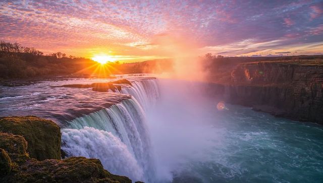 Sunlit waterfall cascading into turquoise gorge at misty dawn with golden sunrise glow