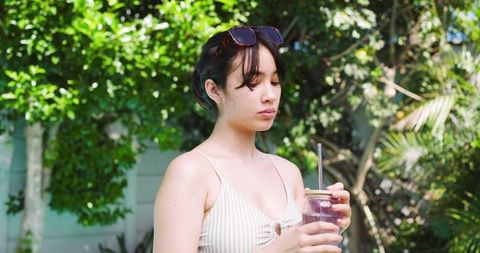 Asian Woman Relaxing in Sunny Garden with Refreshing Drink